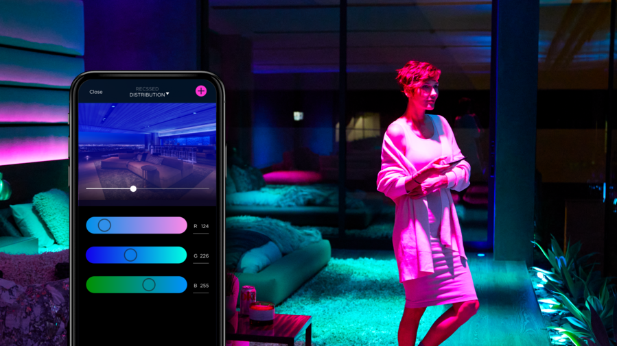 A luxury living room illuminated by smart lights in purple, blue, and green hues, controlled through the Savant app.